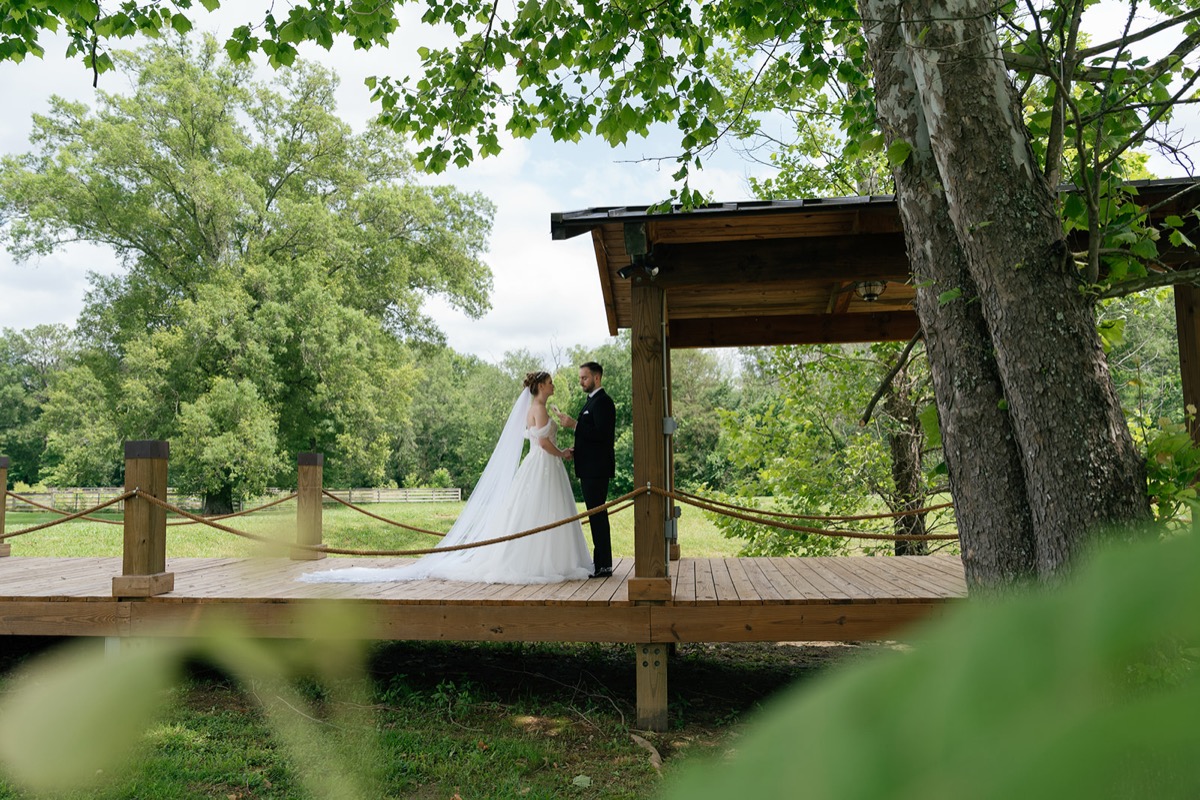 Katelyn & Josh hold hands on Covey Creek’s Pond boardwalk pavilion, veil trailing on the wooden deck