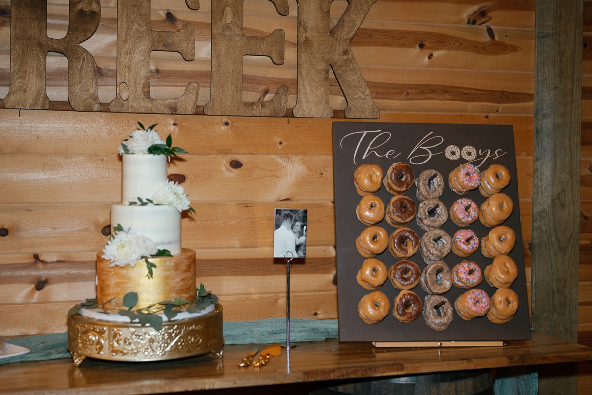 Katelyn & Josh dessert display at Covey Creek: gold-accent cake beside The Booys donut wall indoors