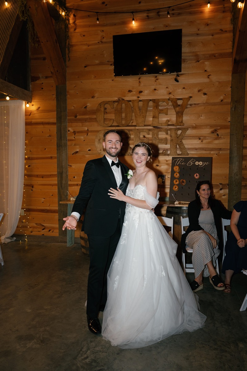 Katelyn & Josh smile before wooden Covey Creek wall letters indoors beside The Booys donut wall