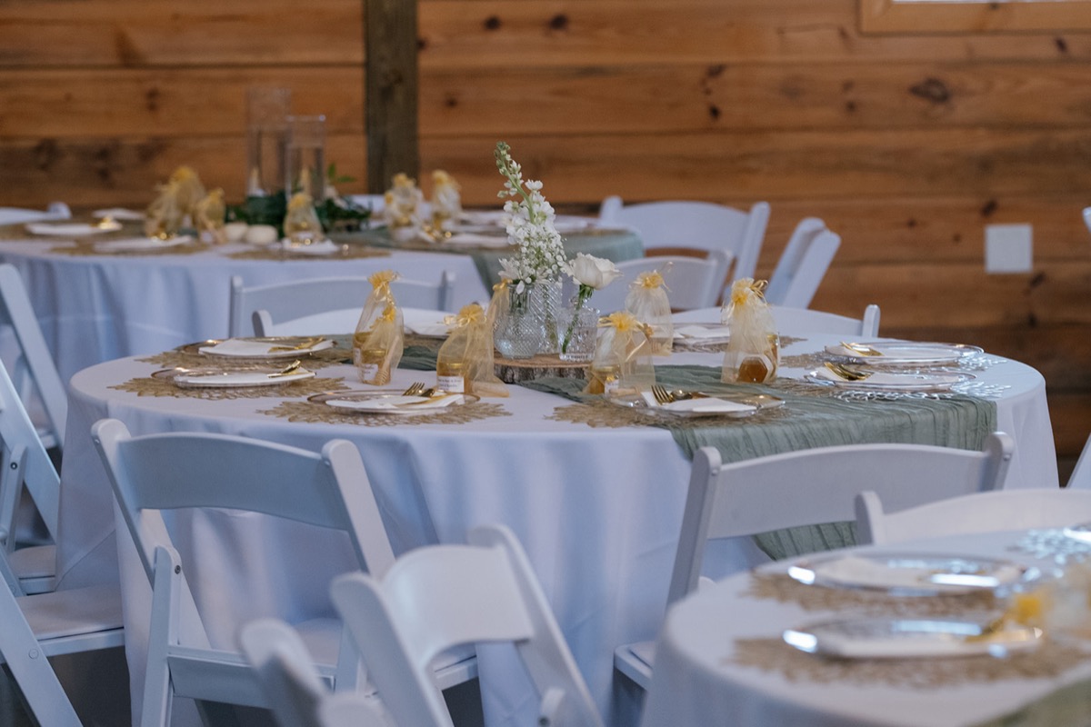 Katelyn & Josh Covey Creek reception table with gold chargers, sage runner, and white bud-vase florals