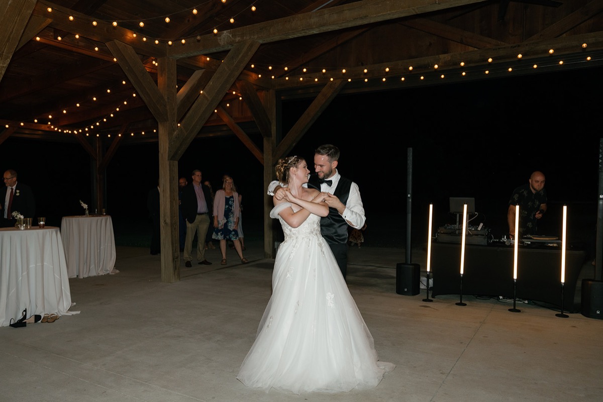 Katelyn & Josh’s first dance under warm string lights in Covey Creek’s timber pavilion at night