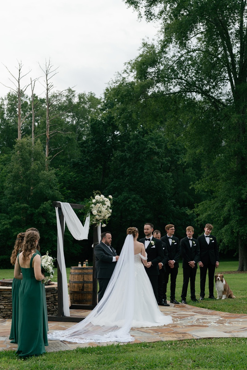 Katelyn & Josh exchange vows at Covey Creek’s Patio under a draped wooden arbor with party and dog