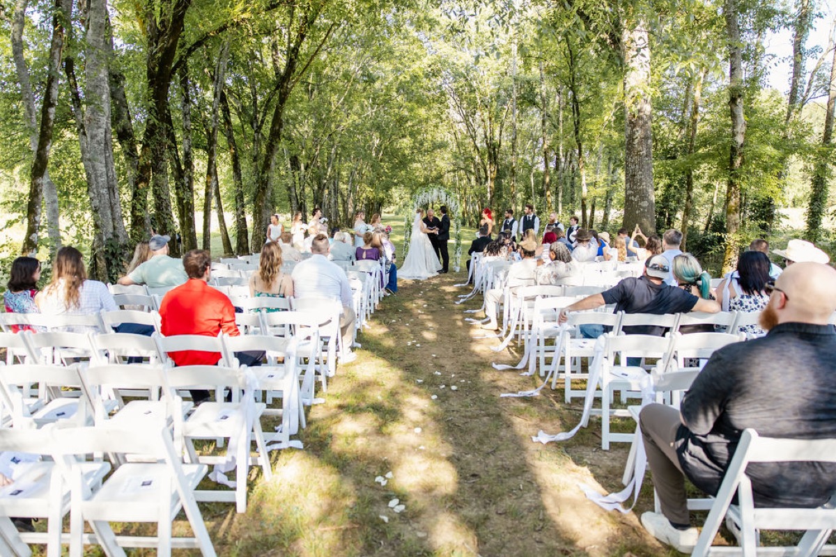 Kolbe & Nathan stand at a white floral arch as guests fill the Tunnel of Love aisle at Covey Creek