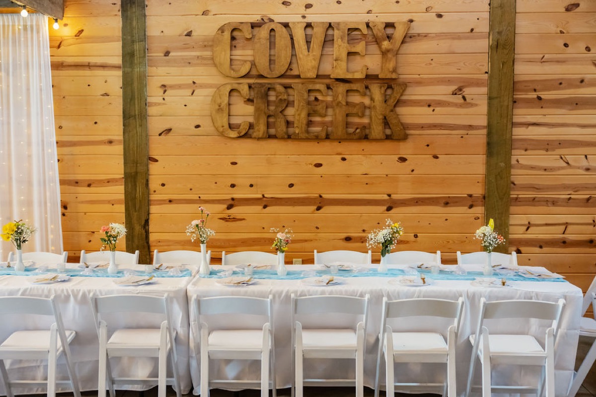 Kolbe & Nathan head table with blue runner and yellow blooms under Covey Creek wood letters indoors