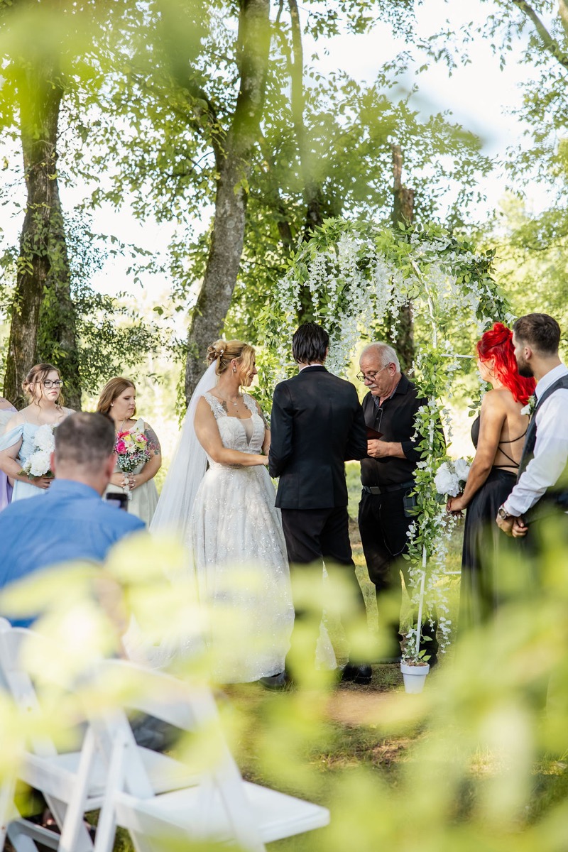 Kolbe & Nathan exchange vows under a white flower arch in the Tunnel of Love at Covey Creek