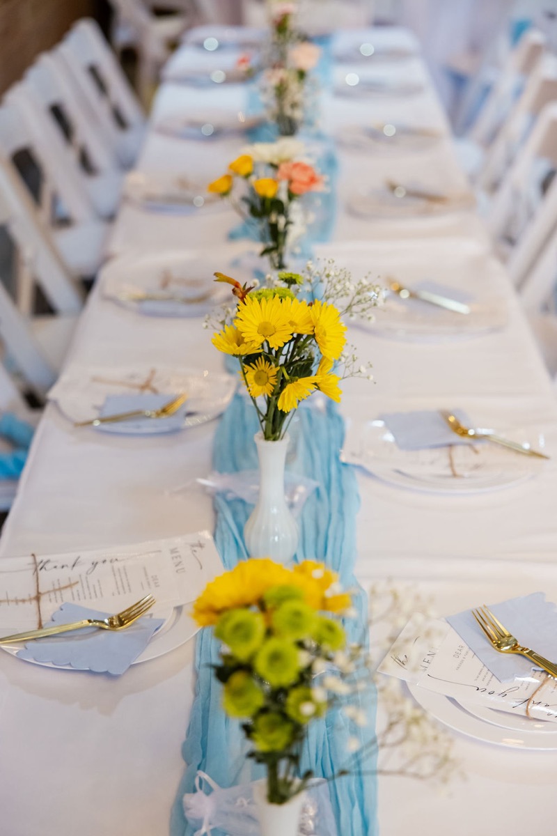 Long reception table with yellow daisies, blue napkins, and thank-you cards for Kolbe & Nathan at Covey Creek
