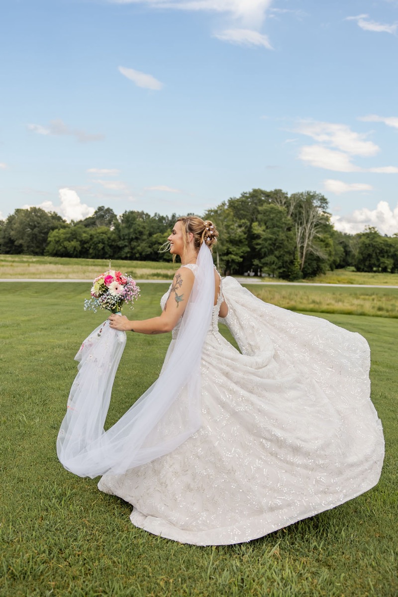 Kolbe spins in her lace gown with veil and pink bouquet on the summer lawn at Covey Creek for Kolbe & Nathan