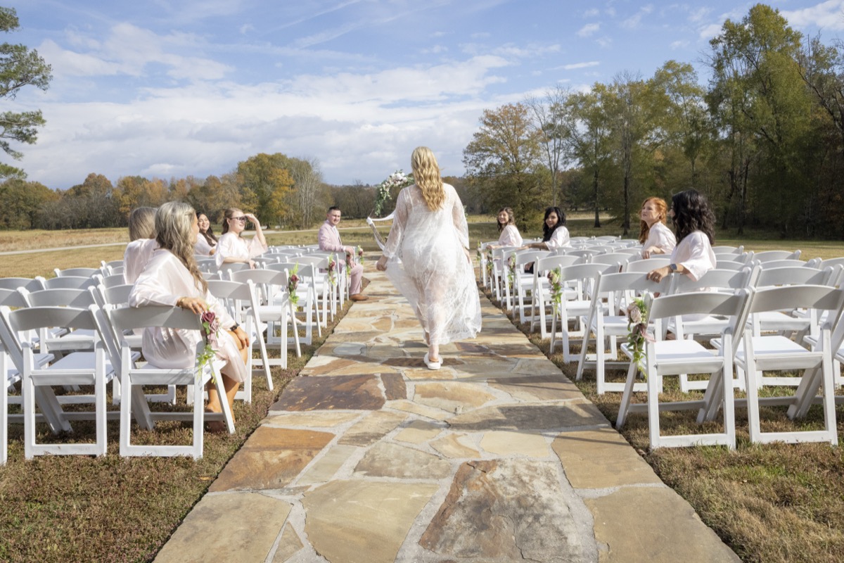 Kristen & Dalton aisle walk in lace robe past bridesmaids in blush robes on flagstone at Covey Creek