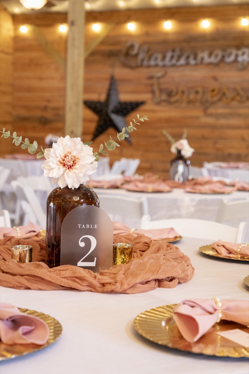 Kristen & Dalton Table 2 centerpiece with acrylic sign, cream dahlia, gold chargers, and rose napkins at Covey Creek