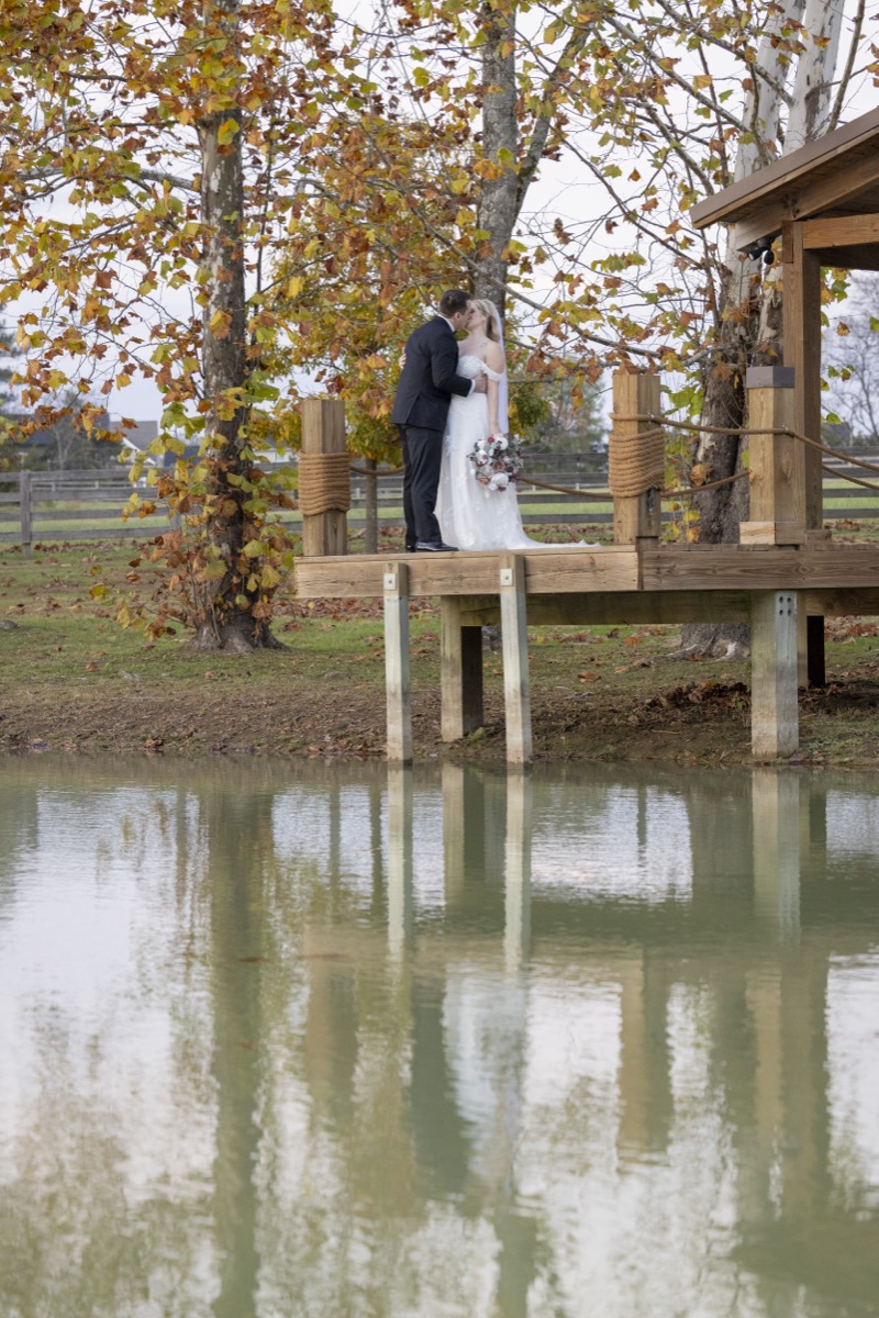 Kristen & Dalton kiss on the Pond dock, their reflection mirrored in still water under autumn trees at Covey Creek