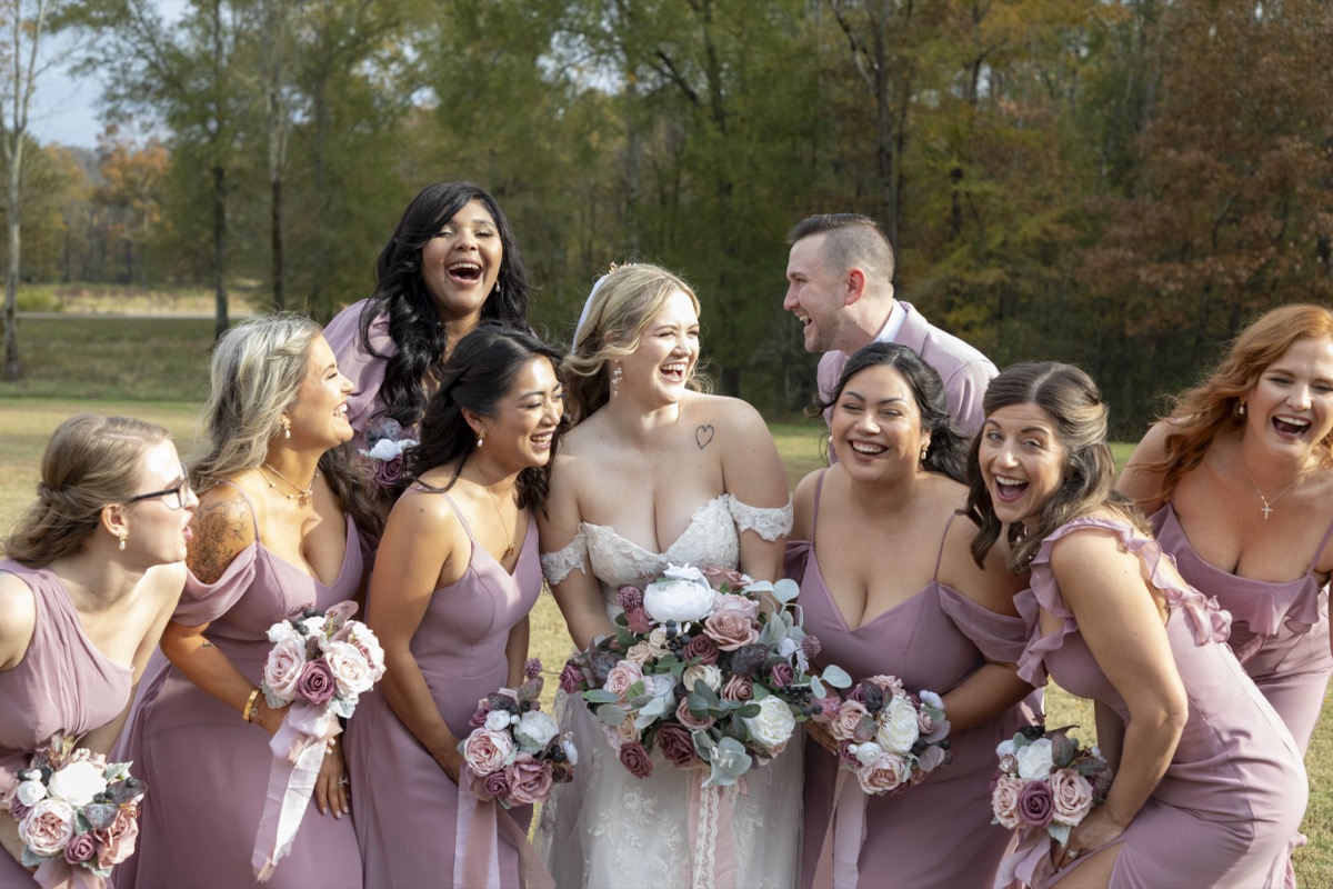 Kristen & Dalton bridal party laughs with mauve dresses and dusty-rose bouquets in a field at Covey Creek