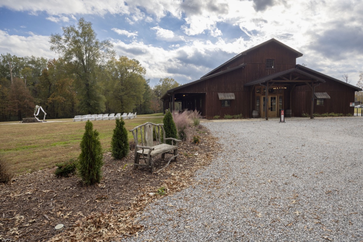 Covey Creek barn exterior with gravel drive, branch bench, and Kristen & Dalton's white-chair ceremony site beyond