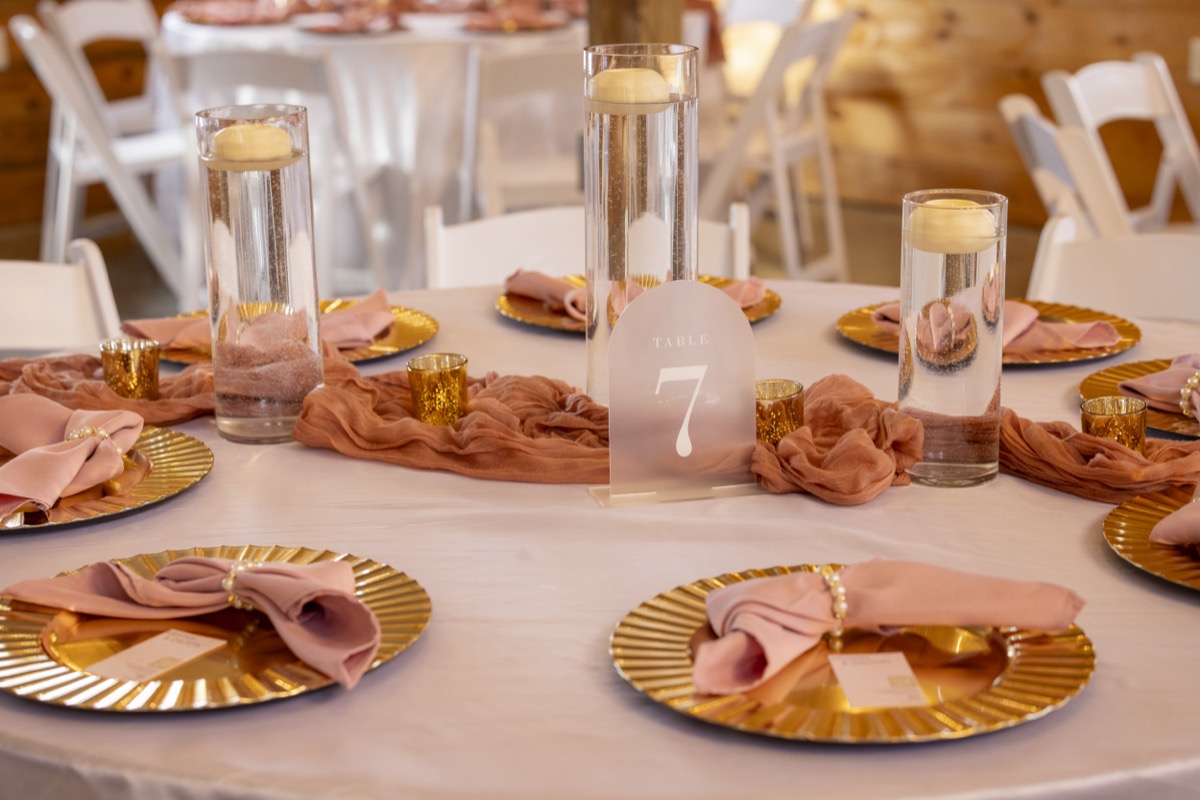 Kristen & Dalton Table 7 with gold chargers, rose napkins, floating candles, and gauze runner at Covey Creek