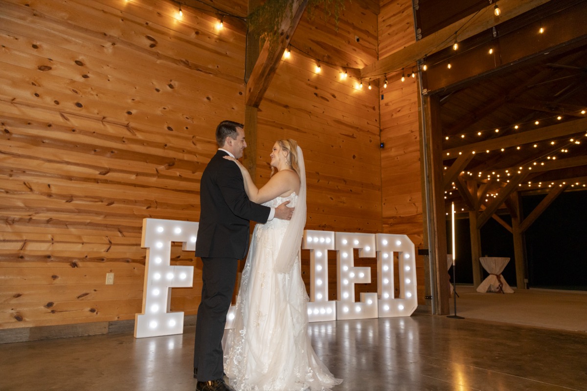 Kristen & Dalton dance before lit marquee letters under Edison string lights in the barn at Covey Creek