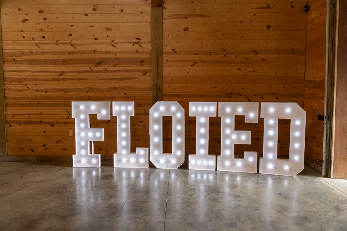 Lit white marquee letters spelling ELOPED glow on the barn floor at Kristen & Dalton's Covey Creek wedding
