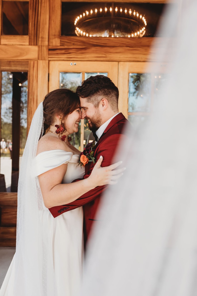 Lauren & Alex press foreheads together by wooden doors, her red earrings bright at Covey Creek