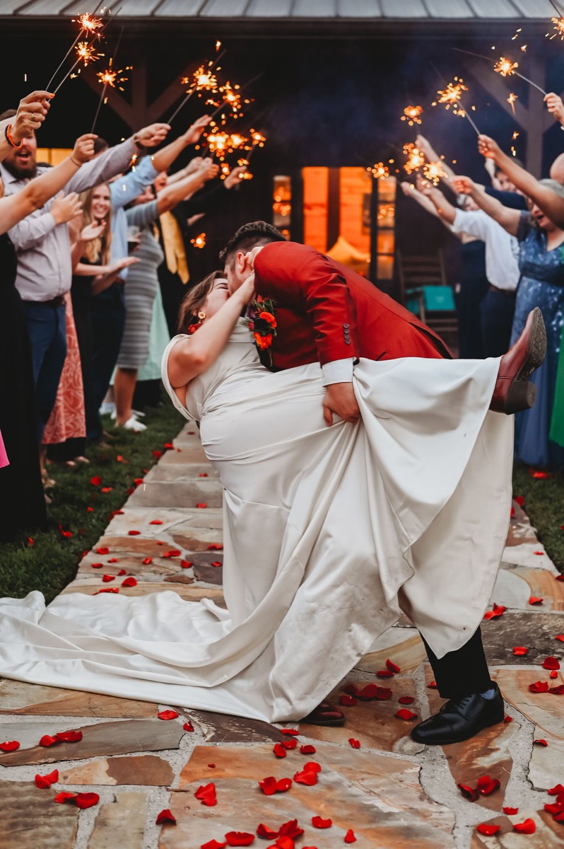 Lauren & Alex share a dip kiss under guest sparklers on a petal-strewn path at Covey Creek