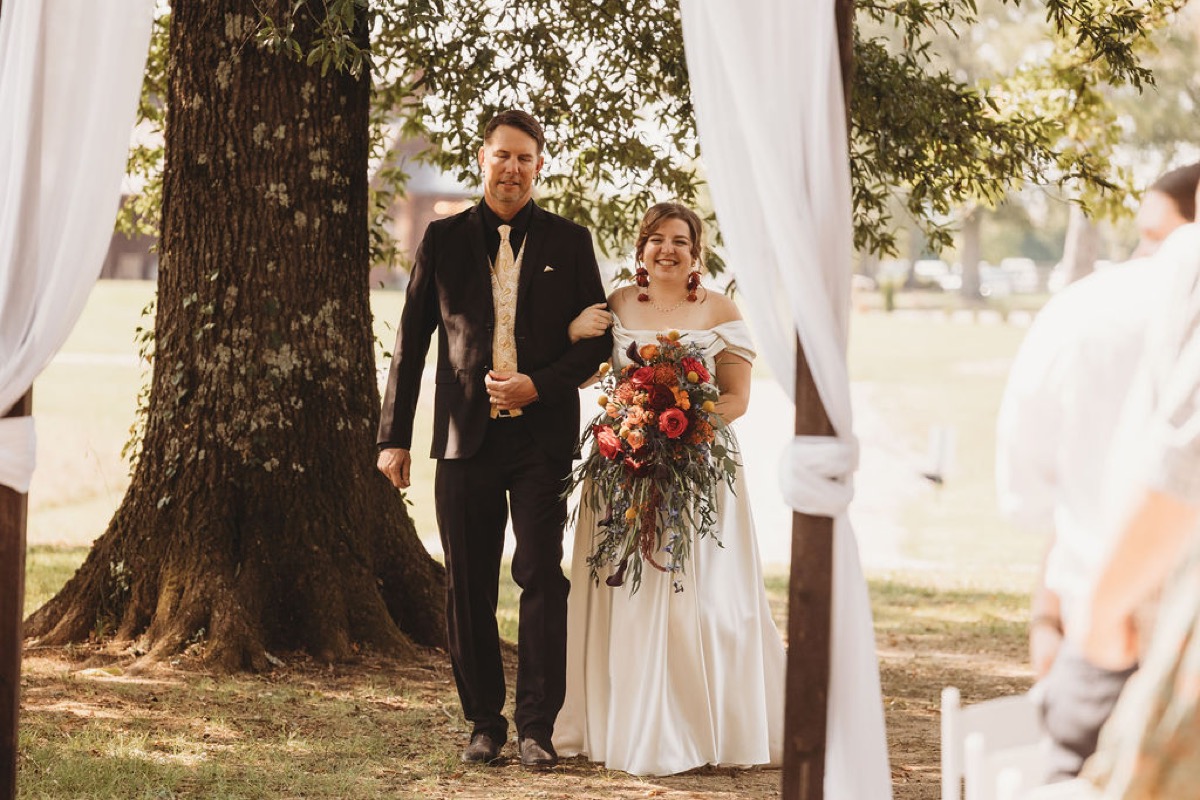 Lauren of Lauren & Alex walks the aisle arm-in-arm with her father holding a fall bouquet at Covey Creek