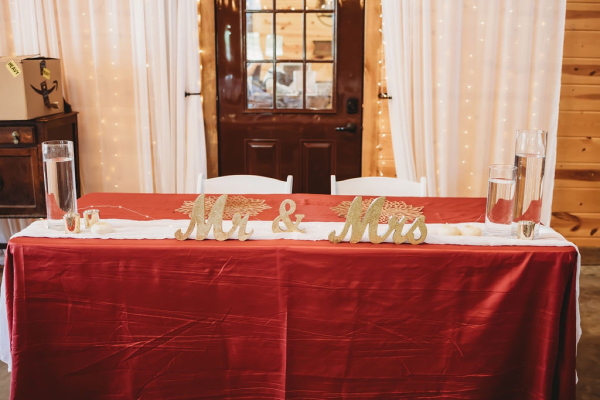 Lauren & Alex's sweetheart table with gold Mr & Mrs signs and red satin cloth at Covey Creek