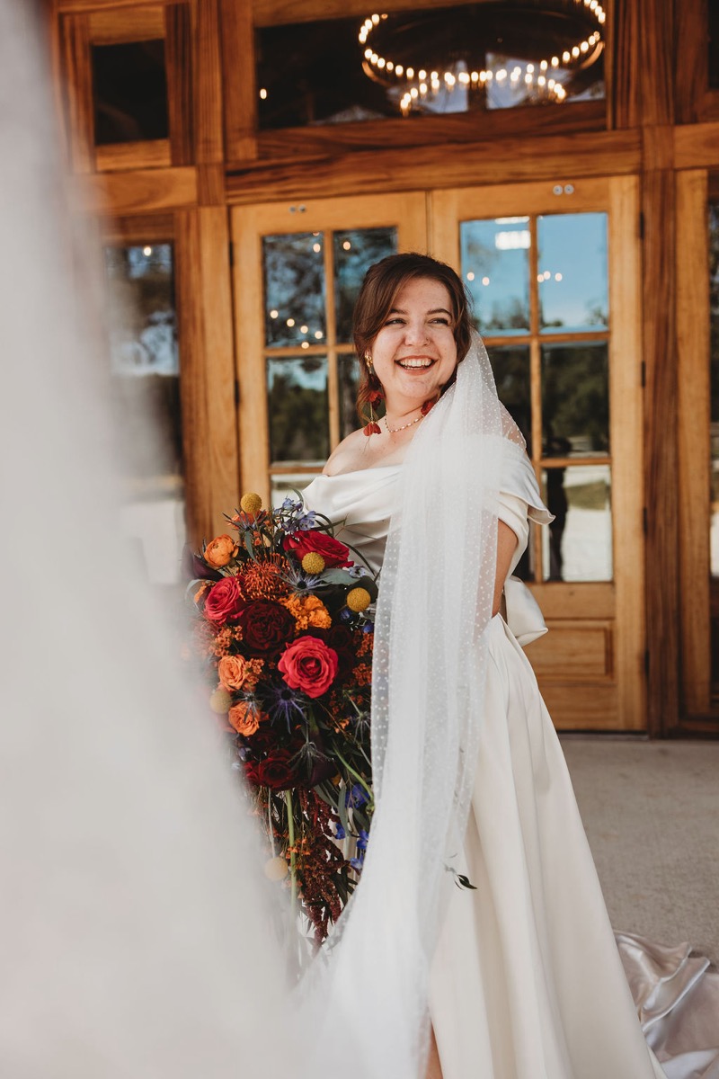 Lauren of Lauren & Alex smiles in a dotted veil with a cascading fall bouquet at Covey Creek