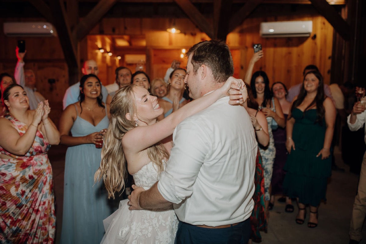 Leah & Gordon smile mid-dance as guests circle them in Covey Creek’s warm wood-paneled reception barn