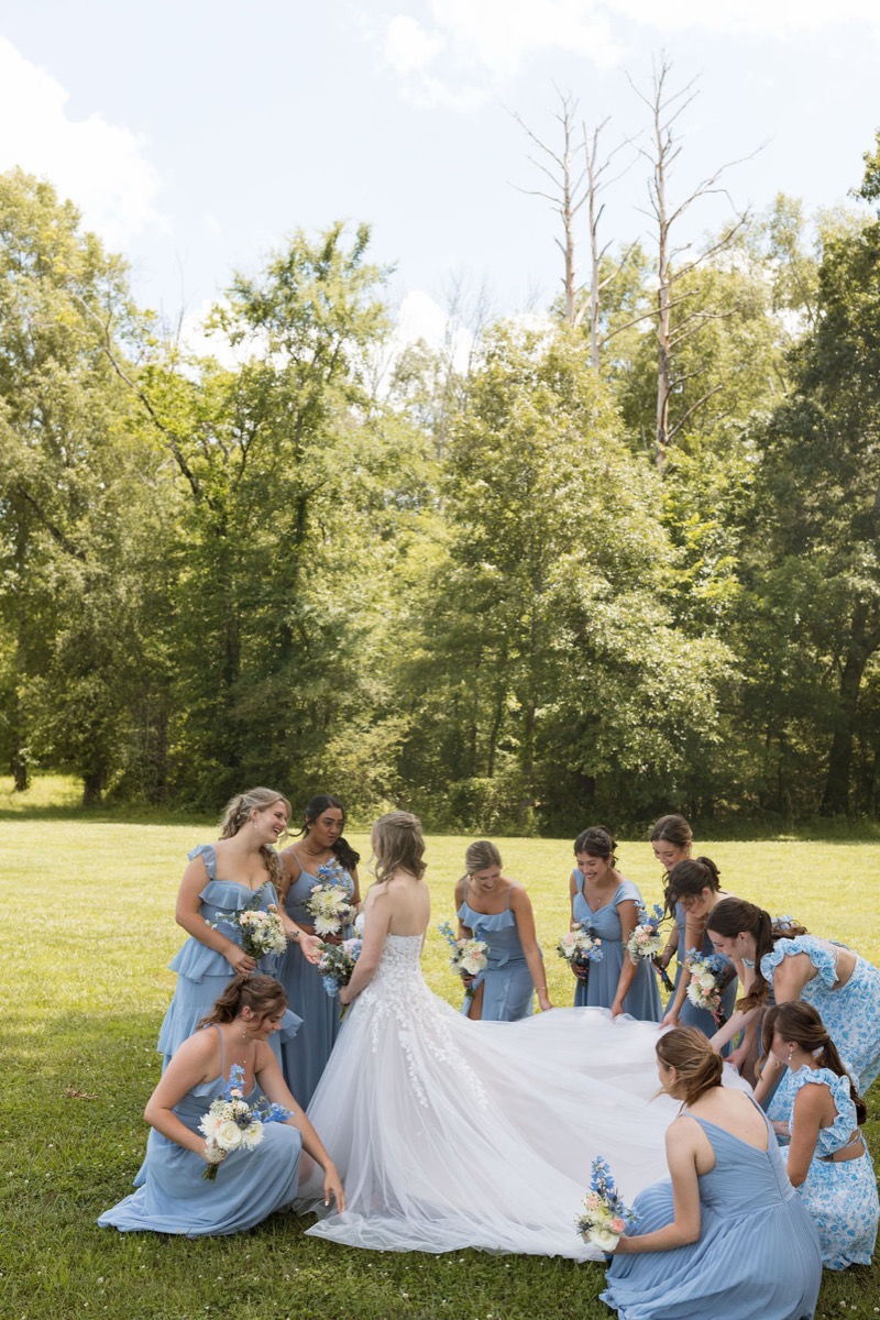 Leah & Gordon bridal party fans out her tulle train on Covey Creek’s green lawn under summer trees
