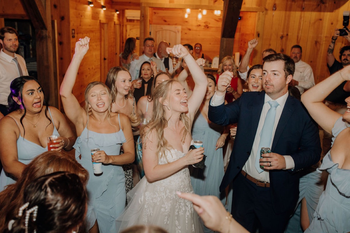 Leah & Gordon dance with bridesmaids in Covey Creek’s wood-walled barn, cans raised mid-celebration