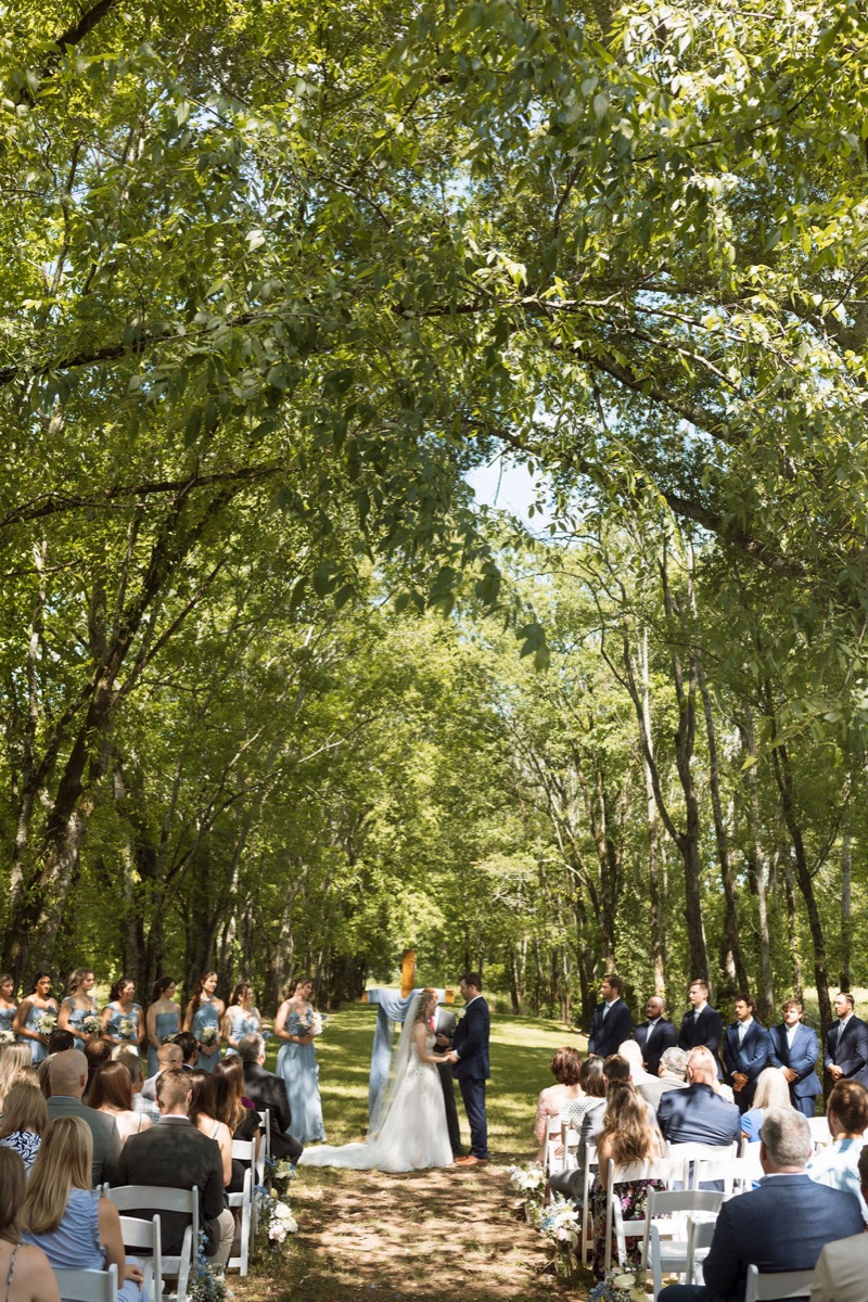 Leah & Gordon exchange vows under Covey Creek’s Tunnel of Love canopy before a blue-draped cross
