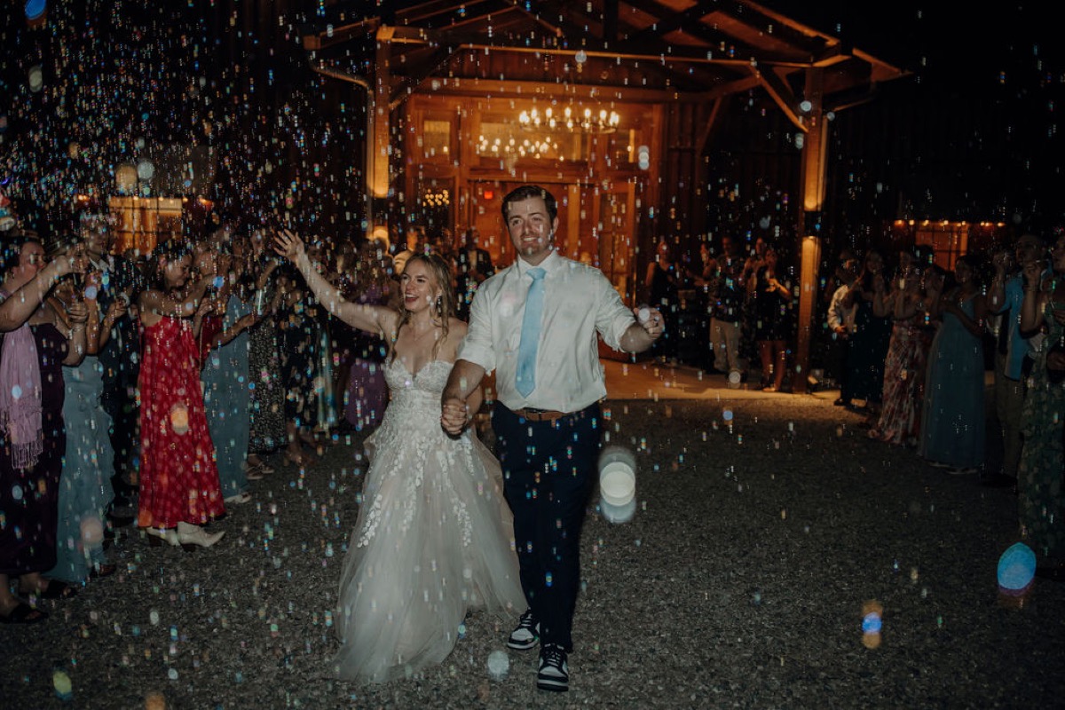 Leah & Gordon walk hand-in-hand through a bubble send-off outside Covey Creek’s lit barn at night