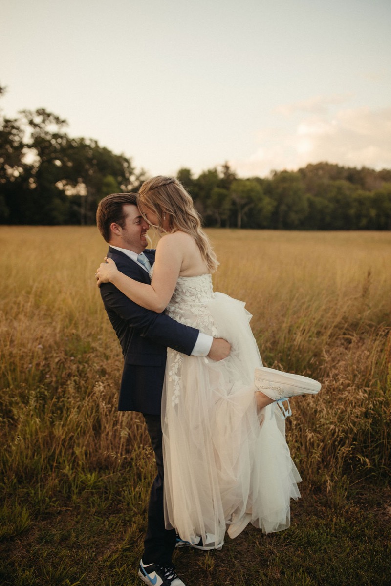 Gordon lifts Leah in a joyful embrace in Covey Creek’s golden field, sneakers and lace gown glowing
