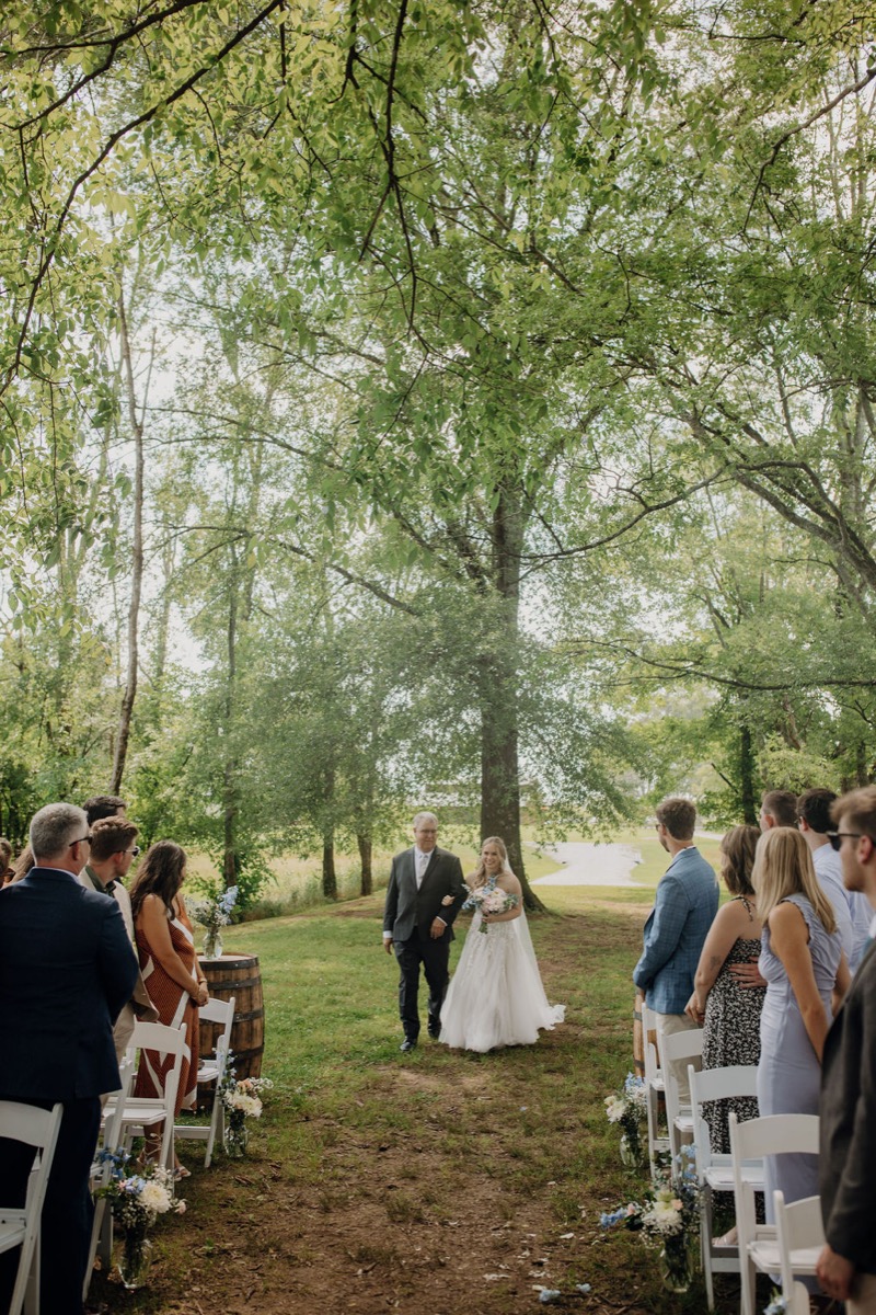 Leah walks Covey Creek’s Tunnel of Love aisle on her father’s arm past guests in white chairs