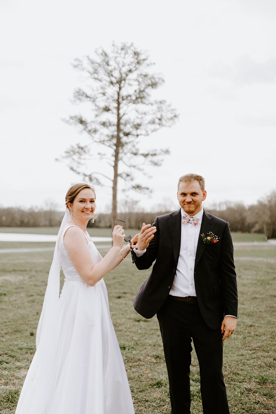 Leslie & Timothy pose with playful handcuffs in a grassy field near the pond at Covey Creek