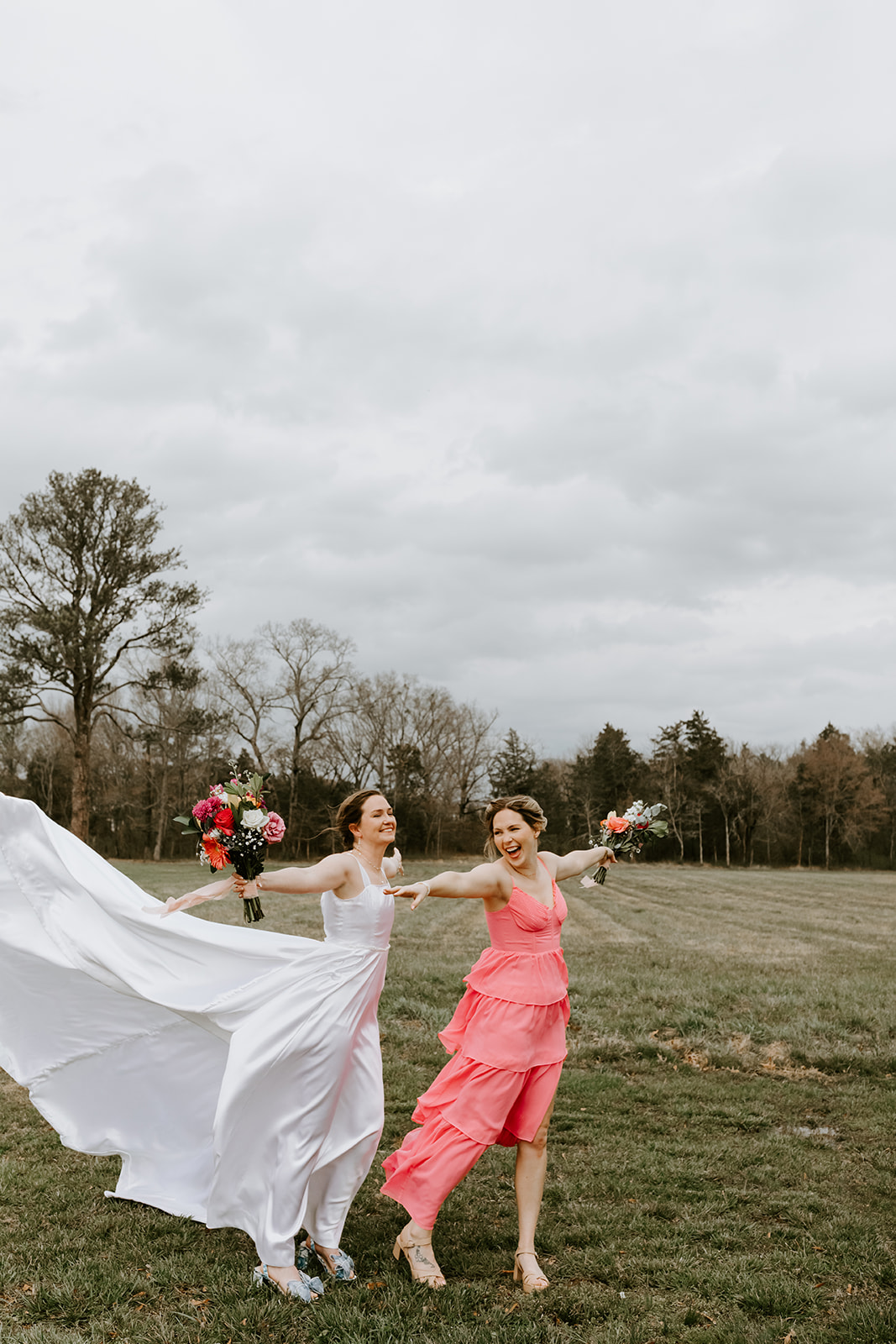 Leslie & Timothy wedding: Leslie runs laughing with coral bridesmaid across Covey Creek field