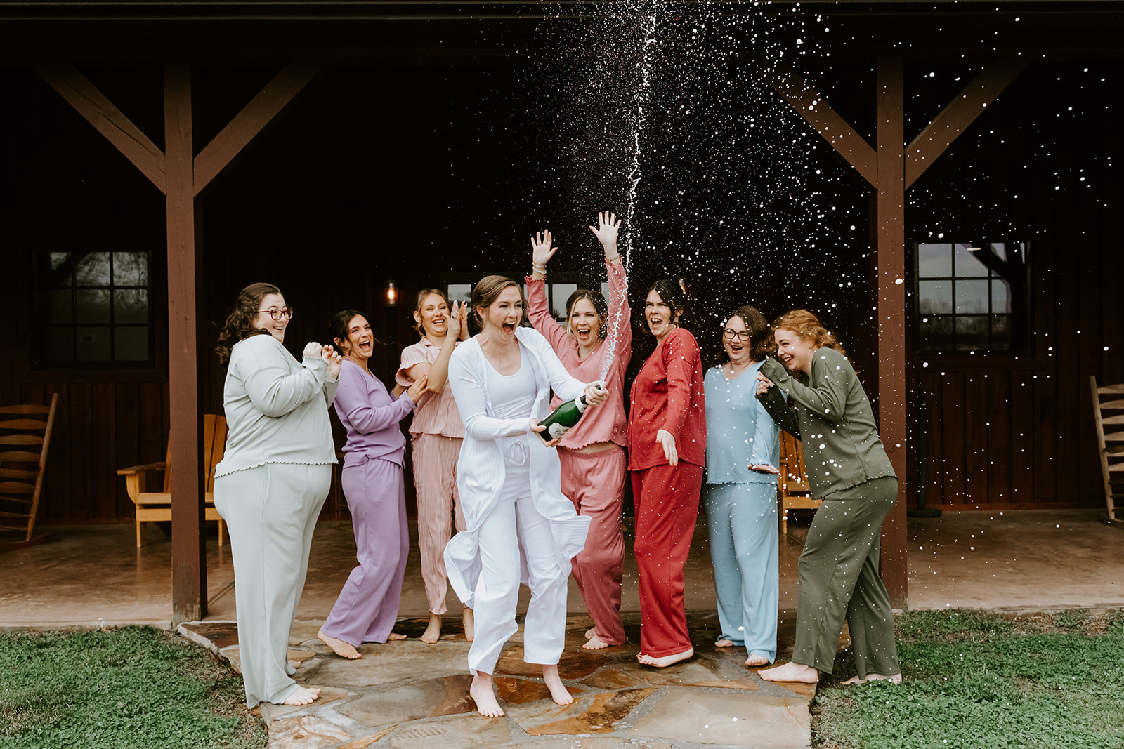 Leslie & Timothy bridal party cheers as Leslie pops champagne spray on the Covey Creek patio