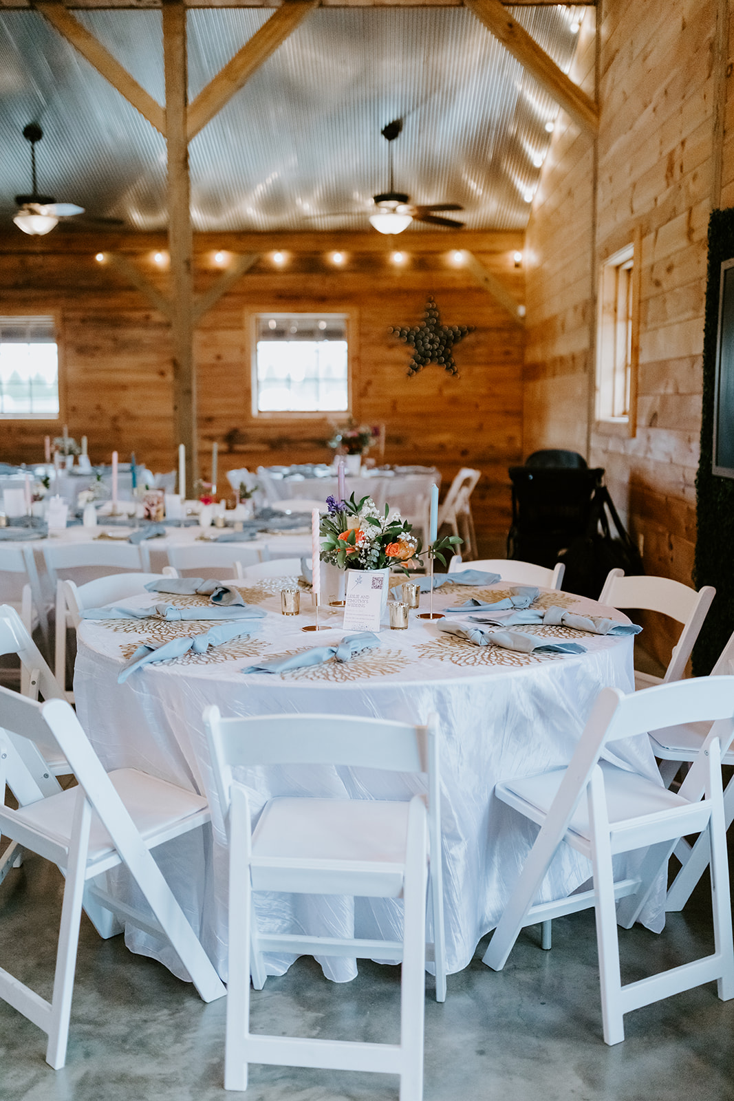 Leslie & Timothy reception table with blue napkins, florals, and candles in Covey Creek barn