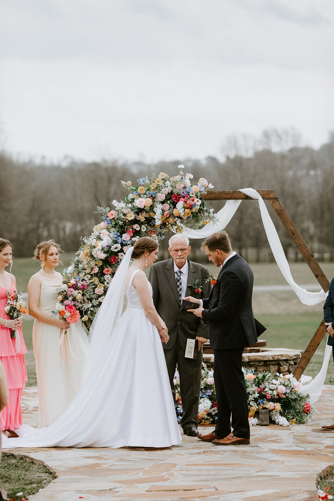 Leslie & Timothy exchange vows with officiant under floral hexagon arch at Covey Creek patio