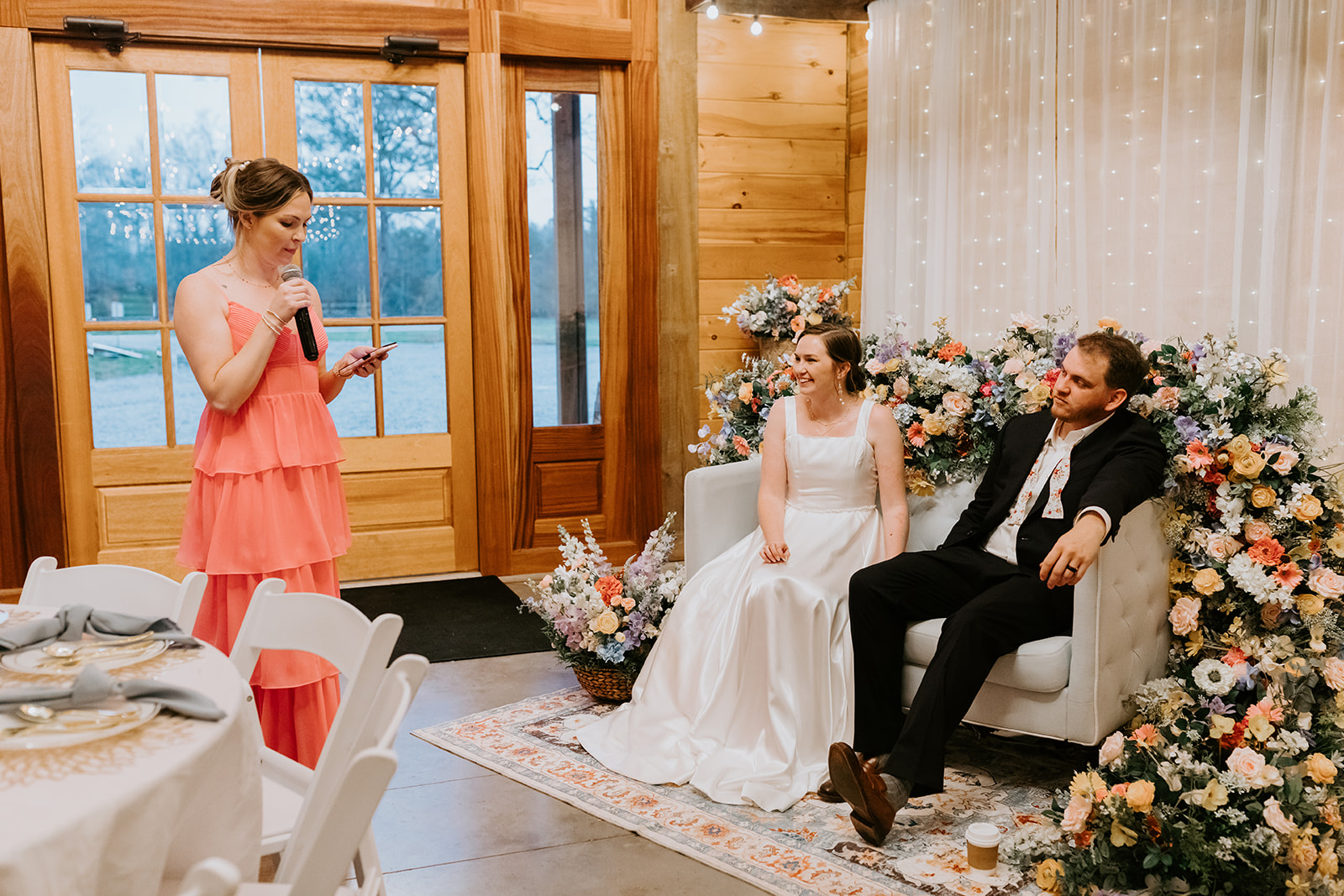 Leslie & Timothy listen to a toast on floral-framed loveseat at their Covey Creek reception