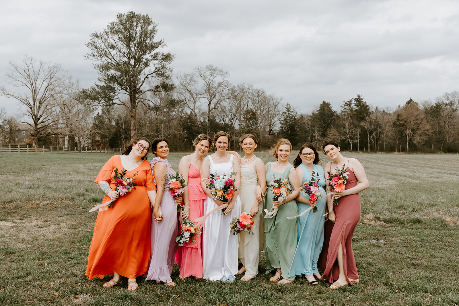 Leslie & Timothy bridal party of seven colorful bridesmaids pose with bouquets at Covey Creek
