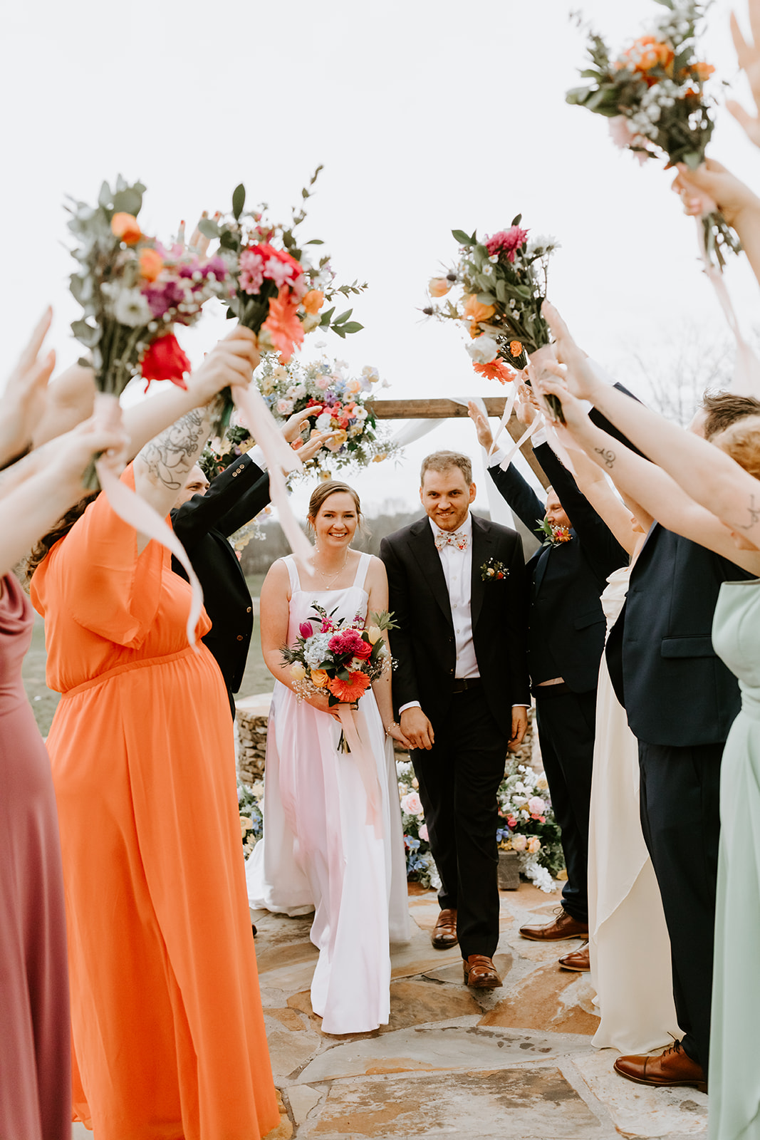 Leslie & Timothy recess under raised arms of their wedding party on Covey Creek flagstone patio