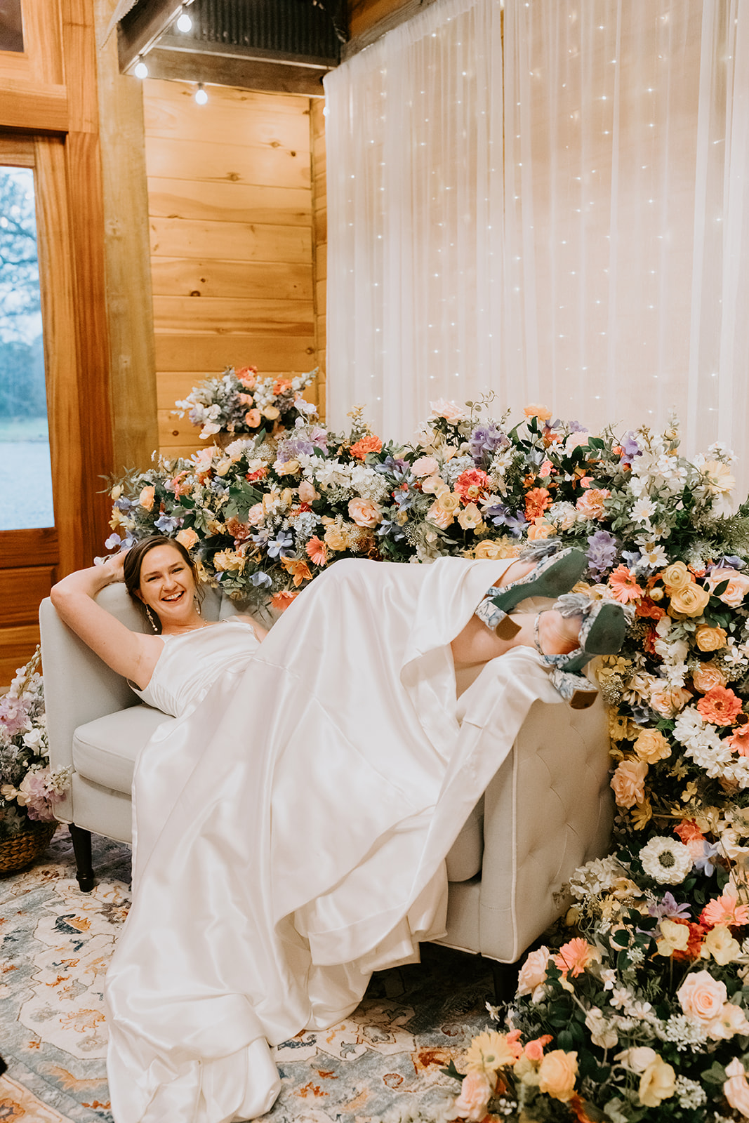 Leslie lounges on tufted settee by floral backdrop at Leslie & Timothy Covey Creek reception
