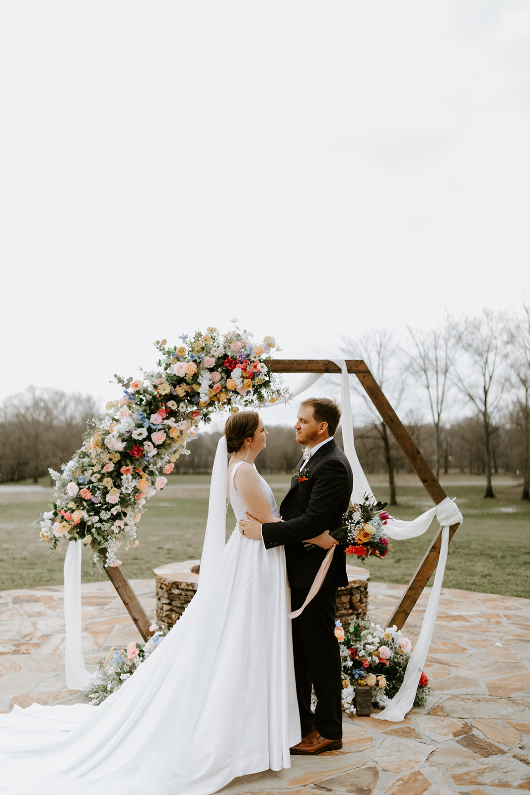 Leslie & Timothy stand face-to-face under floral hexagon arch on Covey Creek patio ceremony
