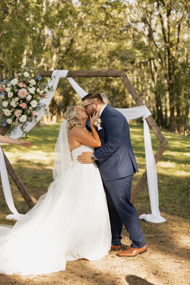 Lilly & Jackson share a first kiss under a floral hexagon arbor at Covey Creek Tunnel of Love ceremony