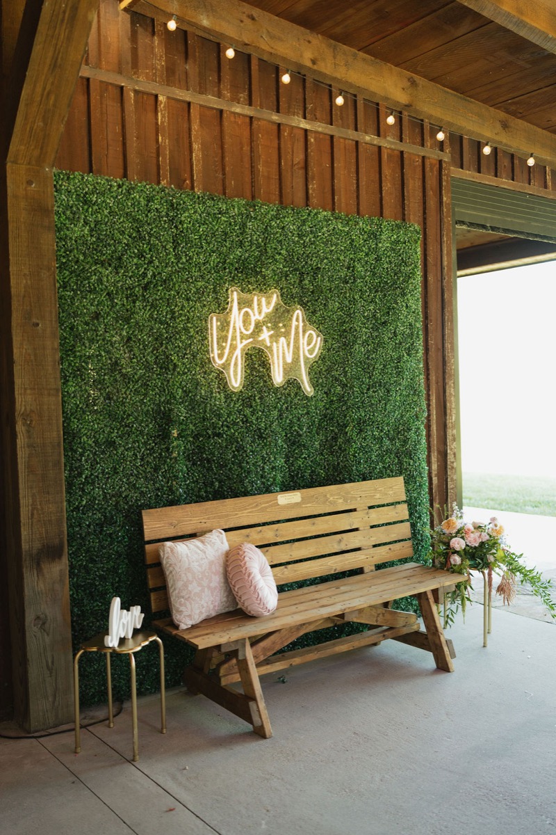 Lilly & Jackson photo booth at Covey Creek with you + me neon, greenery wall, wooden bench, and pink pillows