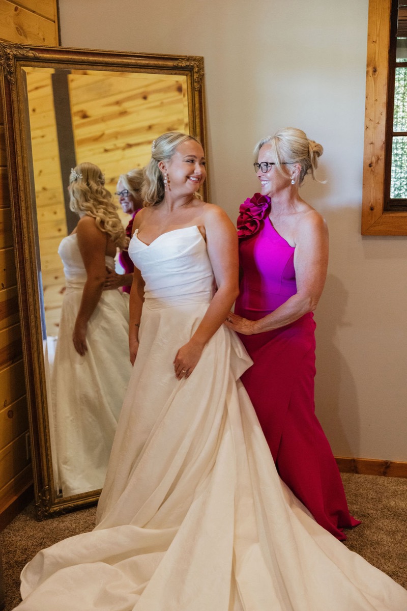 Lilly smiles as a guest in magenta helps with her strapless gown before Lilly & Jackson’s Covey Creek wedding