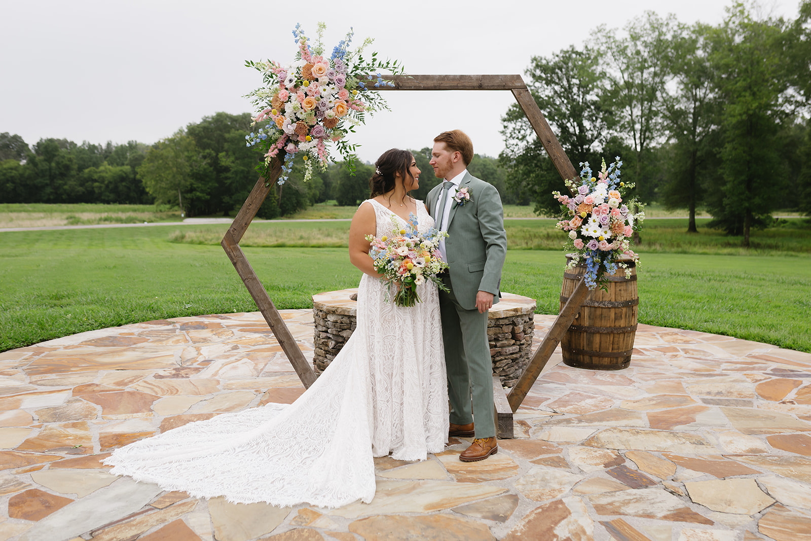 Meredith & Benjamin look at each other under the floral hexagon arch on the Patio at Covey Creek