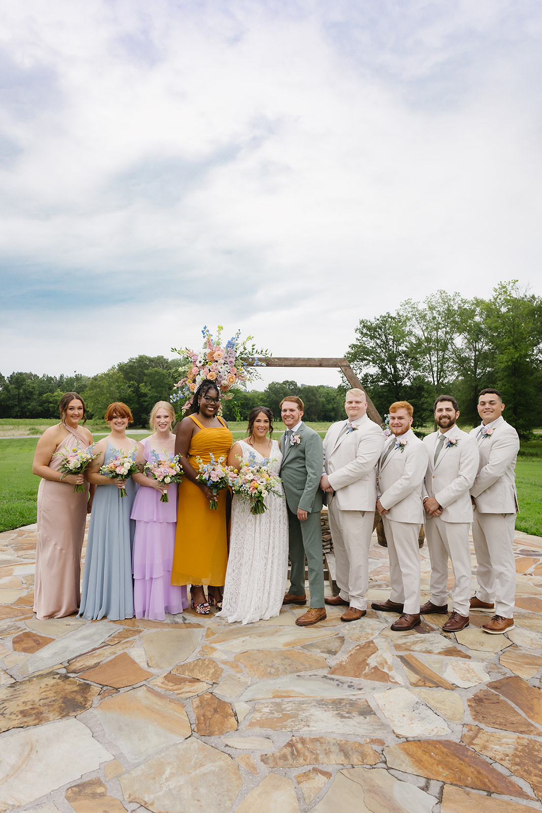 Meredith & Benjamin pose with bridal party in mixed dresses at the Patio arch at Covey Creek