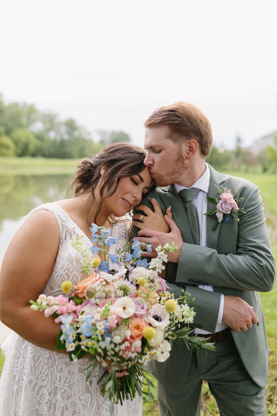 Meredith & Benjamin share a forehead kiss by the Pond with her pastel bouquet at Covey Creek