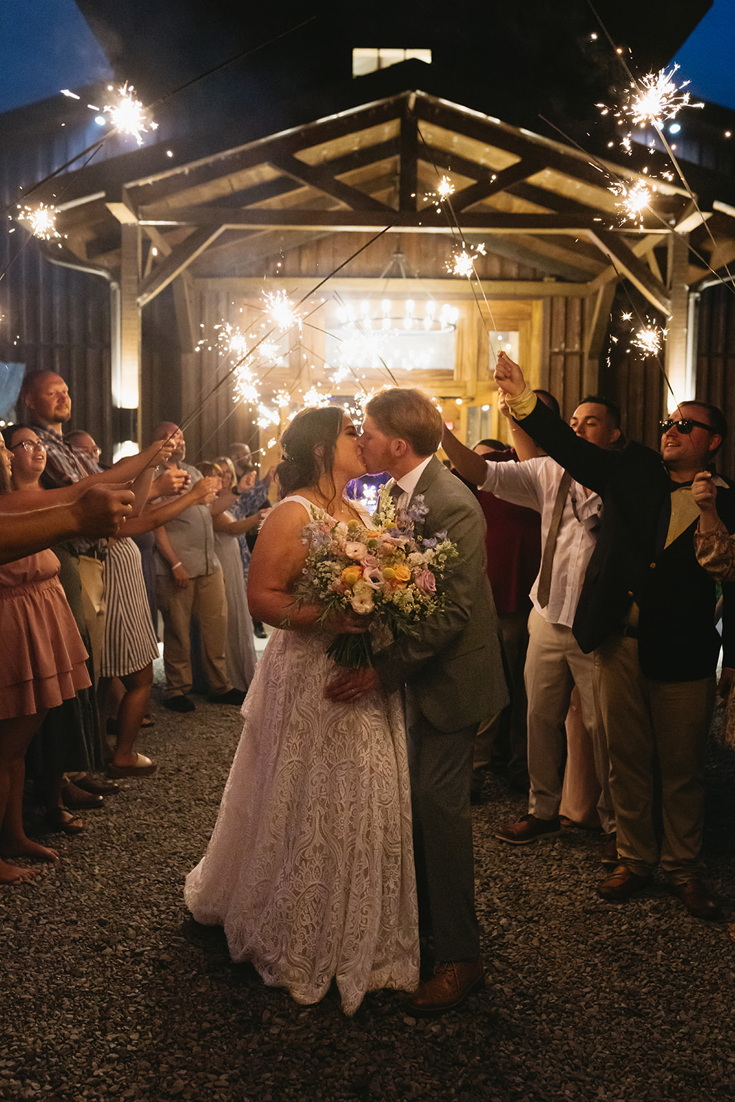 Meredith & Benjamin kiss under sparklers in front of the glowing barn entrance at Covey Creek