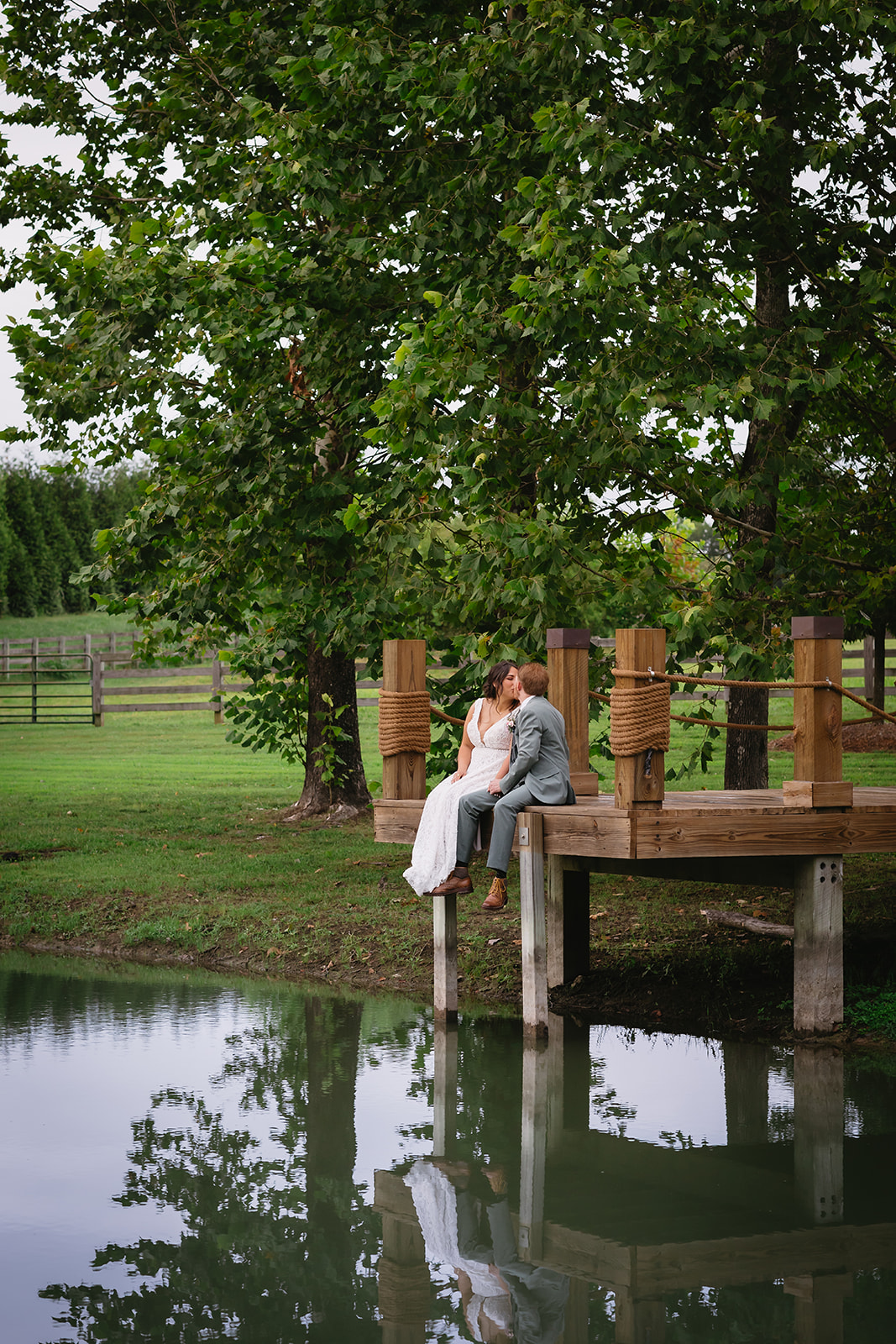 Meredith & Benjamin kiss on the Pond dock with rope rails and water reflections at Covey Creek