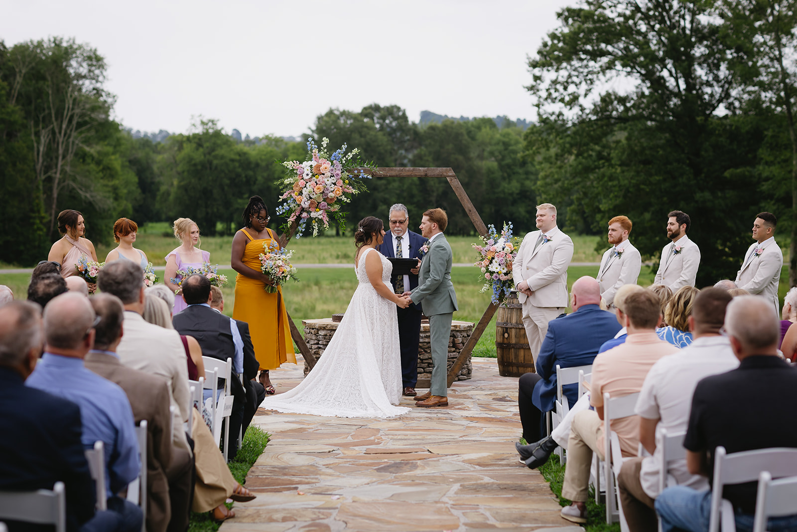 Meredith & Benjamin stand at the floral Patio arch with bridal party and guests at Covey Creek
